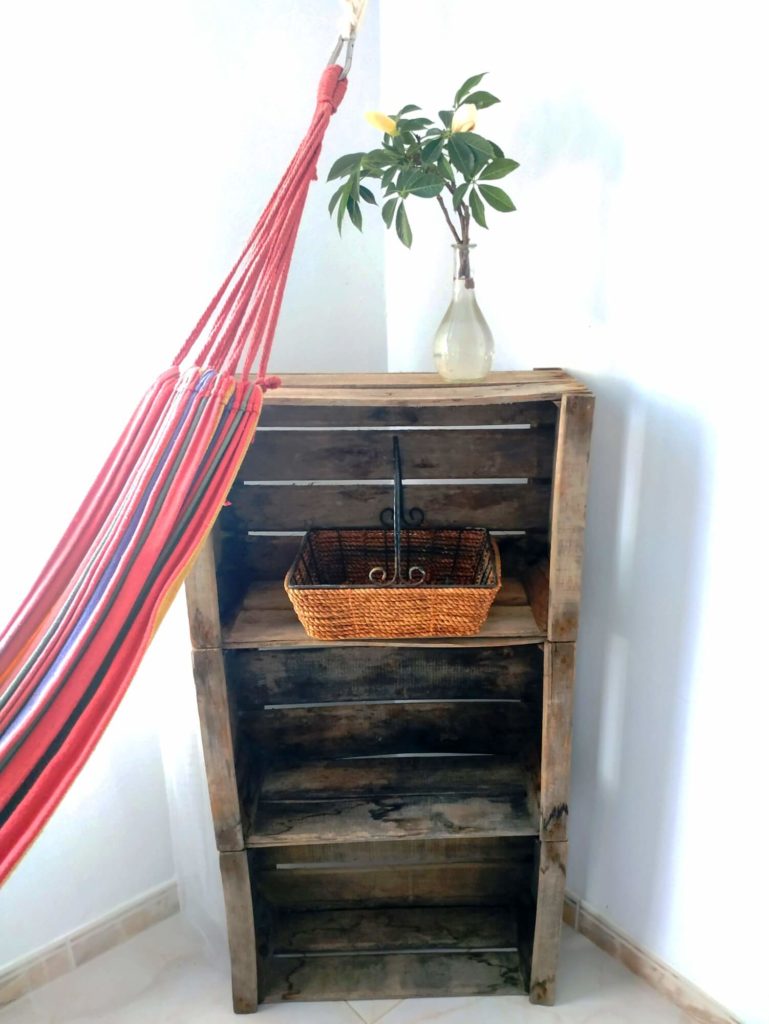 Habitación Tropical hamaca y estanteria de cajas de madera con jarrón de flores