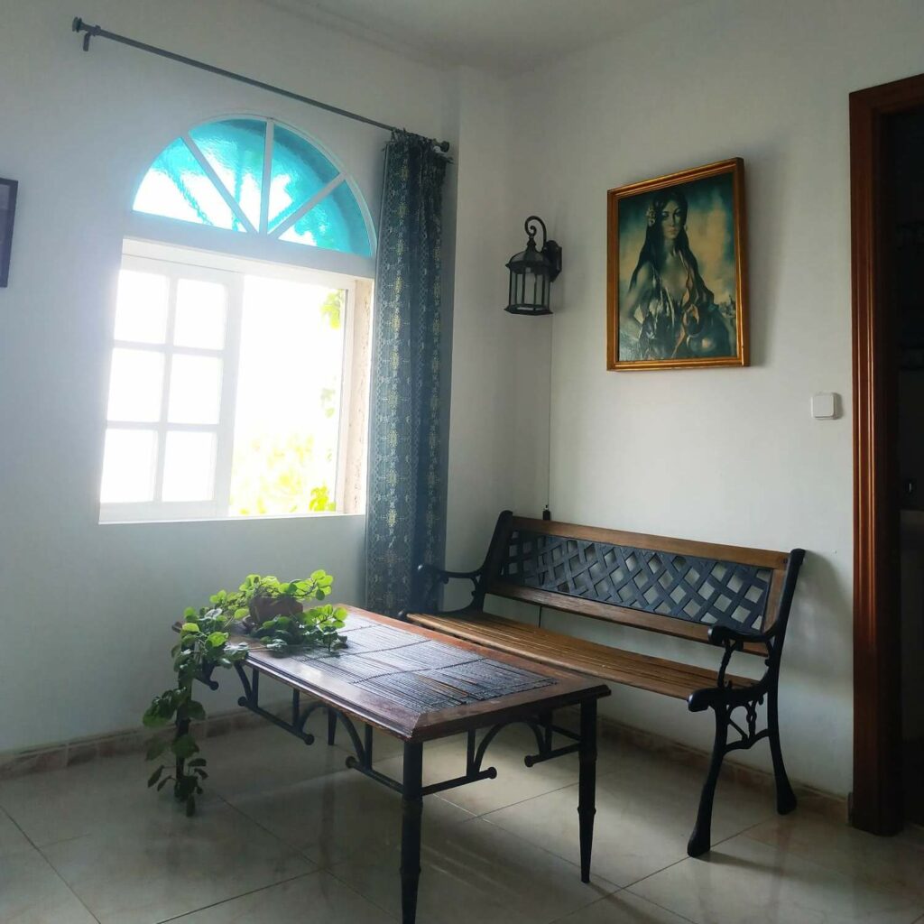 Bright room with a wrought iron and wood bench, a coffee table, a floor lamp and several plants.