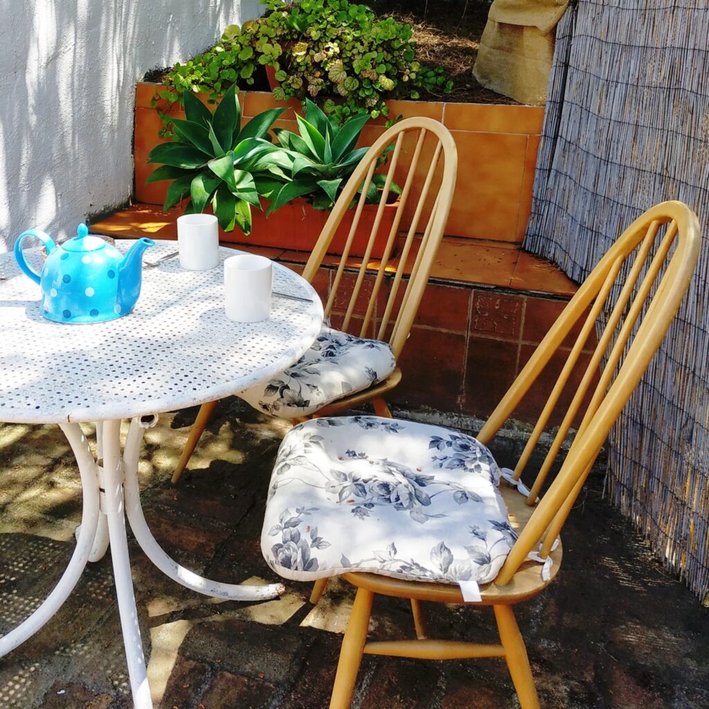 Terras van een wit Andalusisch huis met een witte metalen tafel en rotan stoelen, en planten