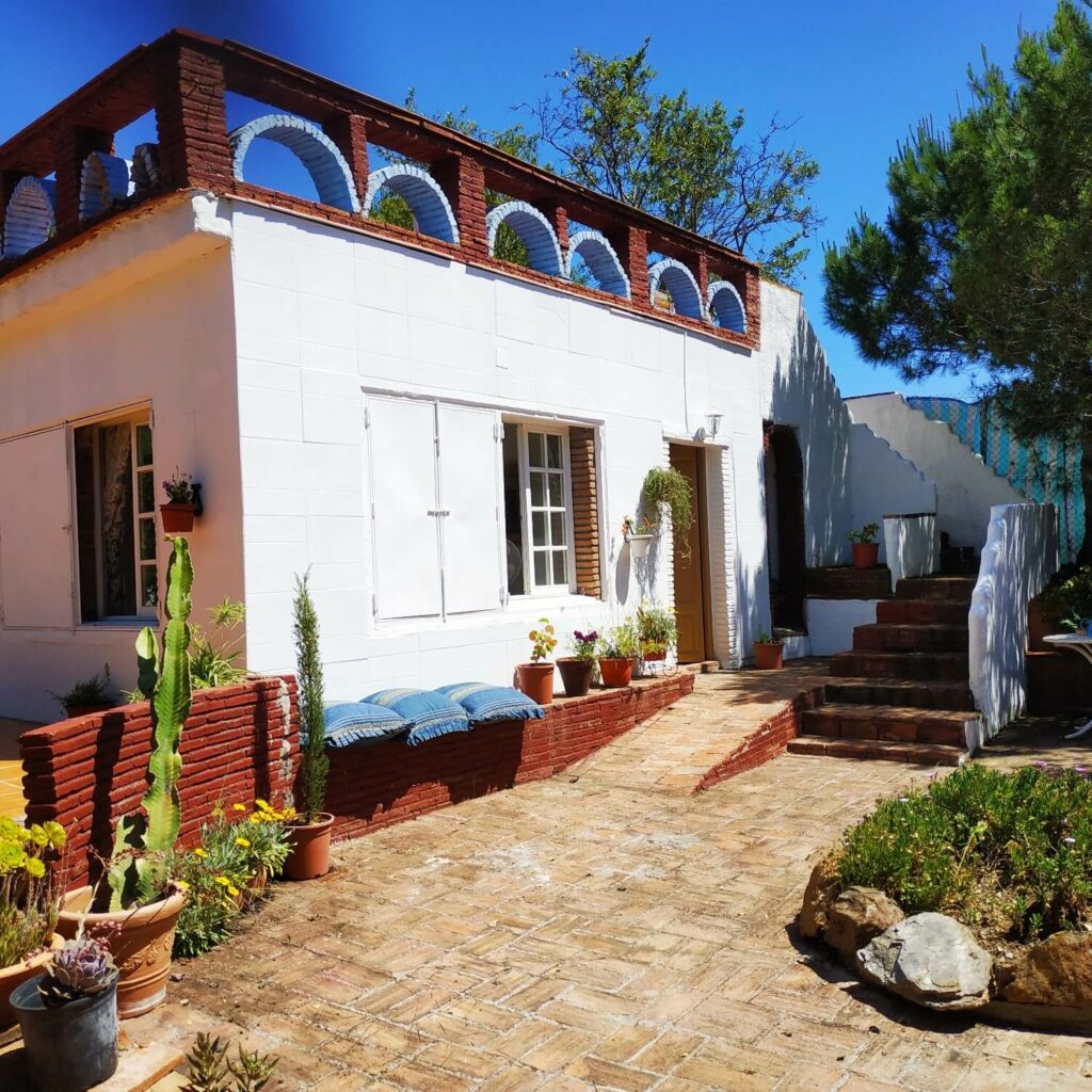 Façade d'une maison blanche andalouse avec des plantes et un escalier au fond