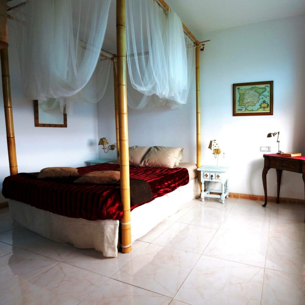 Helles Zimmer mit einem Himmelbett aus Bambus, über dem ein Moskitonetz hängt. An der Wand hängt eine alte Landkarte von Spanien in einem Rahmen.