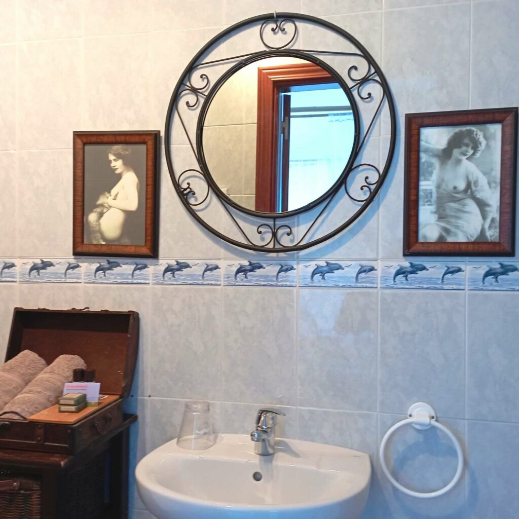 A washbasin topped by a wrought-iron mirror and two Belle Epoque-style photos of women.
