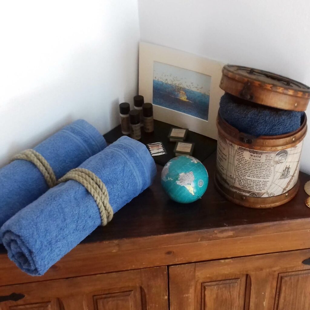 A corner cupboard with two rolled-up blue towels, amenities, a small globe and a box decorated with antique motifs.