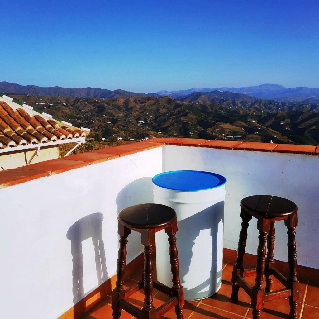 Andalusische Landschaft der Axarquia von einer Terrasse mit zwei hohen Hockern und einem weißen Kanister als Tisch aus gesehen