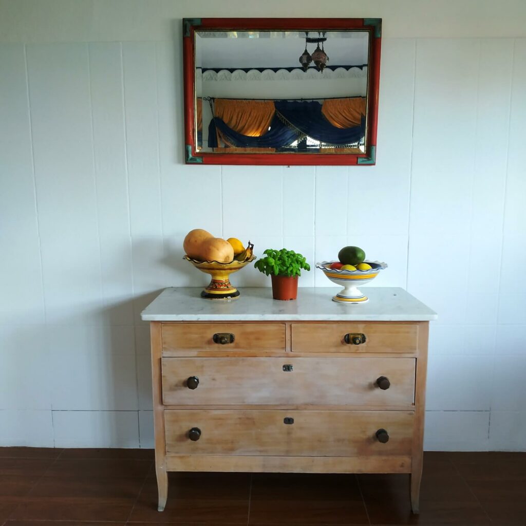 white wall with a chest of drawers containing fruit, vegetables and basil, with a mirror above it