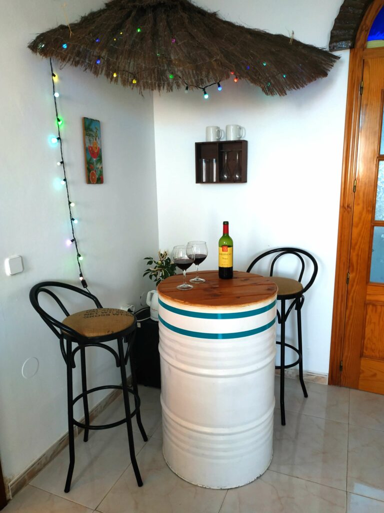 Minibar bestaande uit twee hoge krukken en een wit vat waarop twee glazen rode wijn en een fles staan.