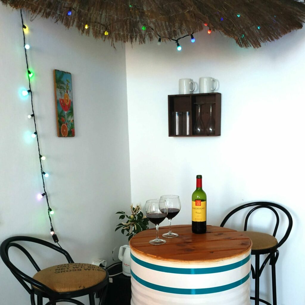Mini bar constitué de deux tabourets hauts et d'un tonneau blanc sur lequel sont posés deux verres de vin rouge et une bouteille.