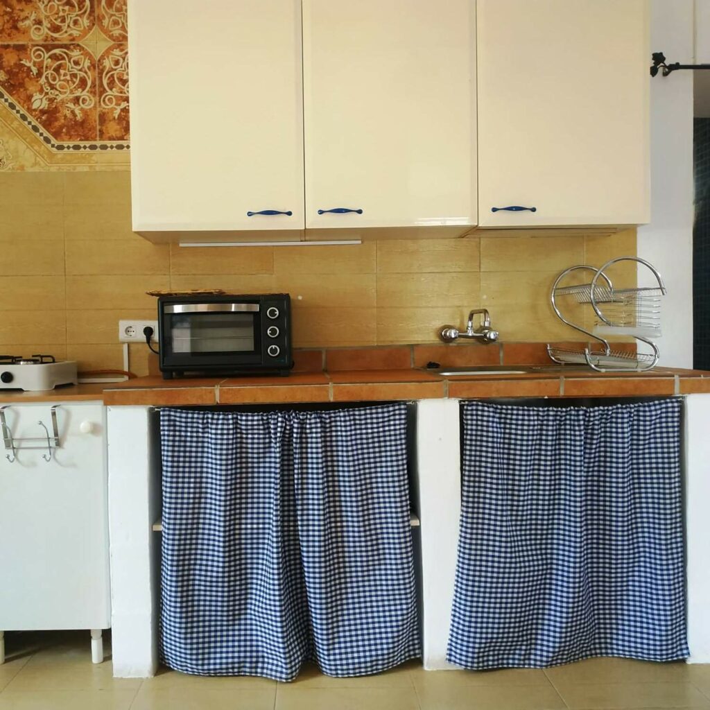 vista frontal de la cocina con un armario blanco en la pared, un fregadero y cortinas de cuadros azules