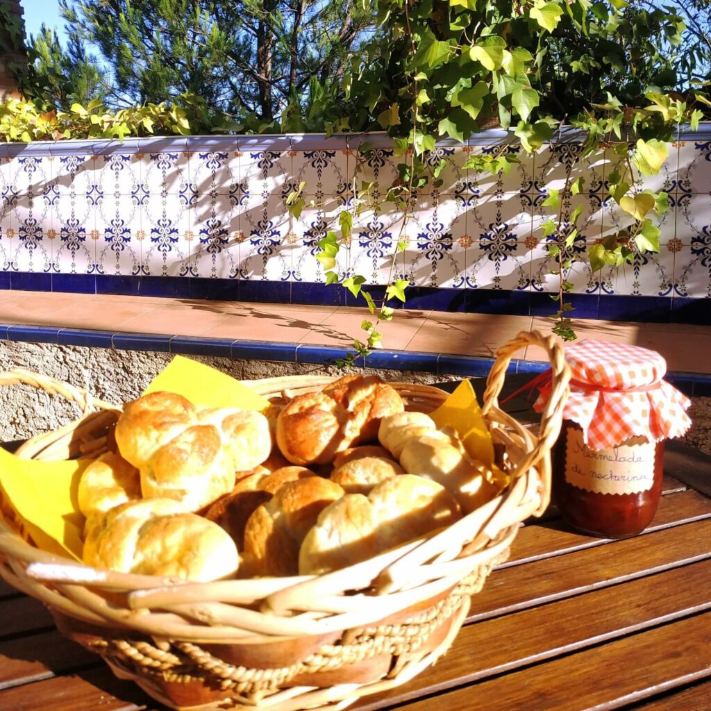 ein Korb mit Gebäck und ein Glas Marmelade stehen auf einem Holztisch auf einer andalusischen Terrasse
