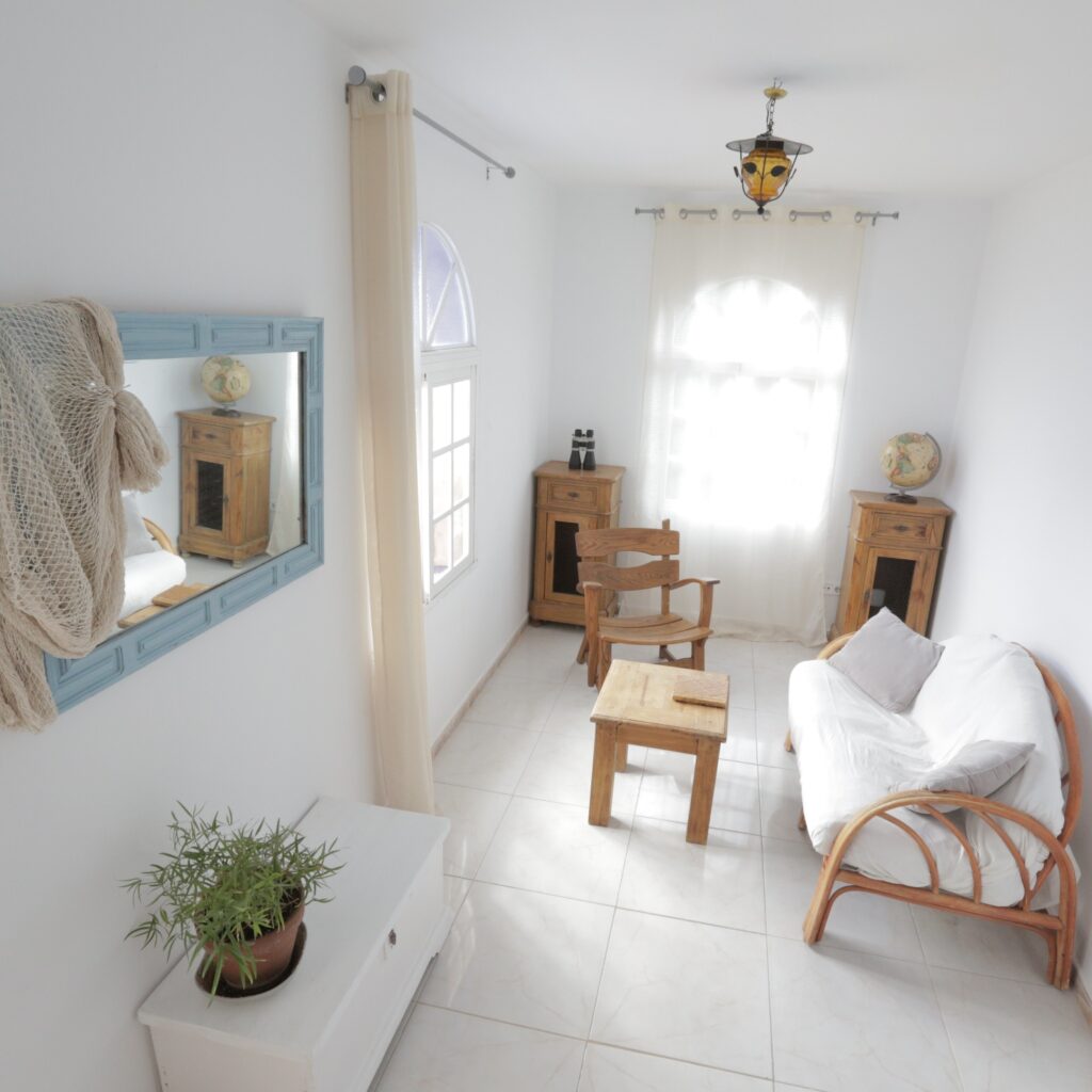 Salón muy luminoso con espejo, mesa de centro y sillón, dos cómodas de madera y un sofá de ratán